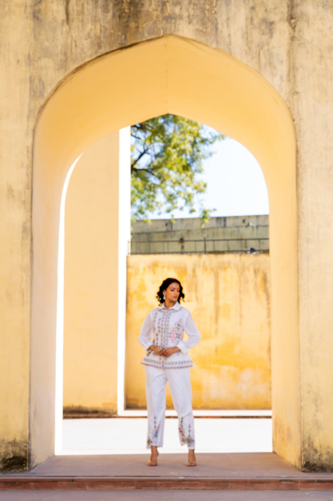 Woman in a white outfit standing in front of a yellow archway with a scenic background