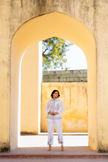Woman in a white outfit standing in front of a yellow archway with a scenic background
